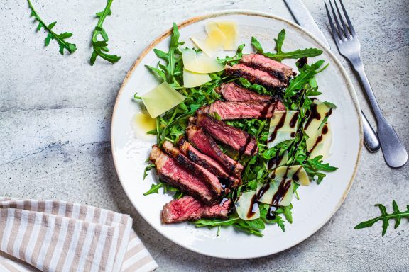 Ein Teller mit aufgeschnittenem Steak, Rucola und Parmesan, mit Balsamico-Glasur.